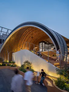 A bustling indoor shopping area with people walking and sitting at tables, surrounded by wood accents and potted plants, creating a warm and inviting atmosphere