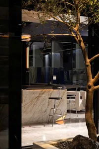 A well-lit living area with a marble kitchen counter, stools, chairs, and a comfortable atmosphere