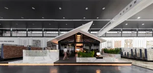 Modern building with a boat-like design, featuring a black roof, large windows, and potted plants, with two people exploring the interior