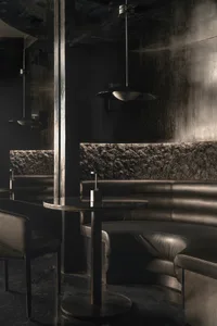 Cozy restaurant or bar area with black leather couches and chairs, stone and wood walls, and a mix of ambient and task lighting