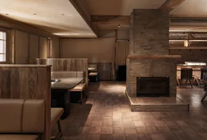 Cozy restaurant or bar space with wooden floors, brick walls, stone fireplaces, and multiple dining tables and chairs