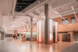 A large commercial space with orange and white walls, columns, and multiple doors, featuring bright lighting and two clocks on either side