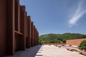Modern building with columns, potted plants, and a mix of concrete and glass elements, illuminated by natural sunlight