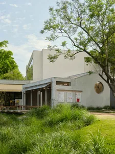 A modern building with a white facade surrounded by greenery, featuring large windows that allow natural light into the space