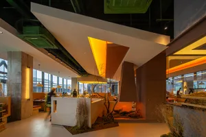 A modern restaurant interior with brown and orange tones, dining tables, chairs, potted plants, and vases, with people present