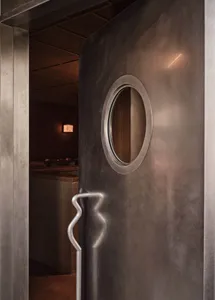 A modern hotel lobby entrance featuring a unique spiral-patterned metal door, surrounded by well-lit space with a sleek atmosphere