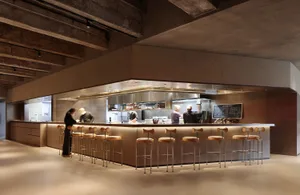 Industrial kitchen with a large countertop, stools, and various cooking and serving items, conveying a functional and efficient atmosphere