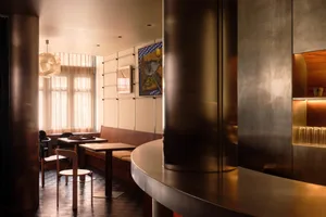Modern bar area with a metal counter, two chairs, and a dining table in a clean and minimalistic setting