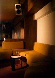 Cozy living space with a yellow couch, brown chair, and a dining table surrounded by seating arrangements, with a wine glass on the table
