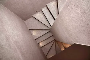 A rendered interior scene of a staircase with concrete steps, lit from above, creating a dark atmosphere