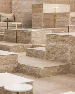 A modern and minimalistic indoor space with stone flooring, featuring steps leading to different levels and couches placed throughout