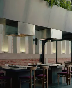 Cozy dining space with brick walls, steel beams, and a modern kitchen with a stove and oven, surrounded by a dining table with various items and potted plants
