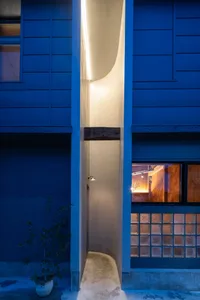 A modern house with a blue exterior wall and a narrow white hallway with two windows and a potted plant near the entrance