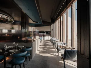 Calm and inviting restaurant with chairs, tables, and wine glasses, set against a backdrop of natural light and large windows