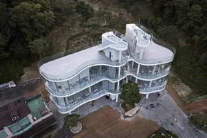 A modern hotel complex with a glass facade, surrounded by trees, and a well-lit interior