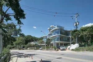 A modern building with a mix of architectural styles, featuring glass windows and a curved structure, set against a predominantly white background, with parked cars on the street