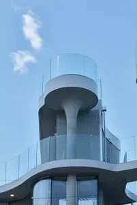 A sleek modern building with a glass structure, featuring windows and balconies, set against a neutral background