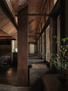 Warm and inviting interior space with wooden beams, pillars, and furniture, featuring a potted plant and comfortable seating arrangements