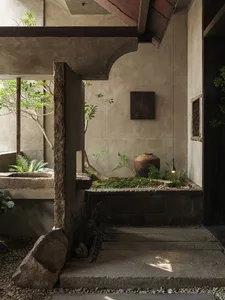 A calm and inviting indoor space with a stone wall, large window, potted plants, and a vase, emphasizing natural and organic design elements
