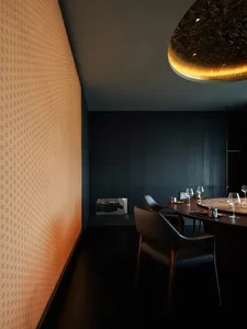 A dark dining area with a black table and chairs, set with wine glasses, creating an intimate atmosphere