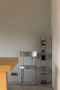 Empty living space with a wooden dining table, a silver metal chair, and two small shelves on the wall
