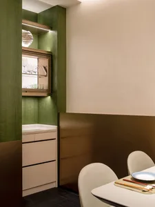 A kitchen with green walls, white cabinets, and a dining table in the background, featuring wine glasses and scattered cups