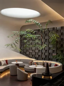 Comfortable living space with a circular seating arrangement, multiple couches, chairs, and dining tables, surrounded by neutral colors and sleek lines, with potted plants adding a touch of greenery