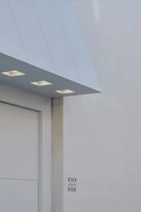 Exterior building with a white concrete wall, a gray door, and several wall lights creating a well-lit atmosphere