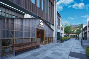 A wooden building with a large window and two wooden benches in front, set in a calm and inviting environment