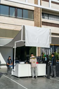 An outdoor cafe with white canopies, tables, and chairs, featuring a casual atmosphere and lively public space