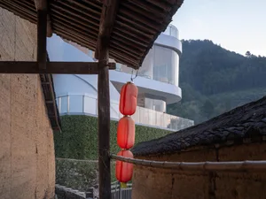 Asian-style building with a wooden roof, stone wall, and three red lanterns, set in a peaceful and serene environment