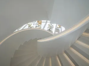 A luxurious spiral staircase in a museum with white marble steps, chairs on multiple levels, and a sense of elegance and sophistication