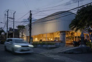 A modern building at night with a white car driving by and people walking around outside, surrounded by wires and a lively atmosphere
