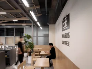 casual indoor café setting with wooden tables and chairs, potted plants, and a person sitting on a chair