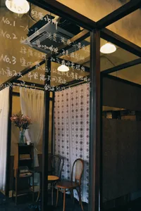Cozy Asian-style living space with a wooden door, two chairs, a table, and a vase, dimly lit for a warm atmosphere