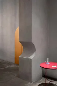 A cozy interior space with a red table, candle, and concrete walls, featuring two doors and a modern industrial feel
