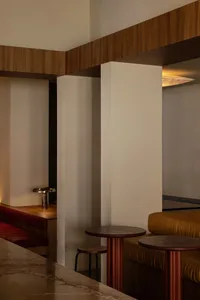 A modern living space with a bedroom and dining area, featuring two couches, chairs, and a dining table, with white walls and wood furniture, illuminated by natural light