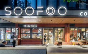 A modern outdoor cafe with a wooden facade, chairs, and a lively atmosphere, with a dog walking past