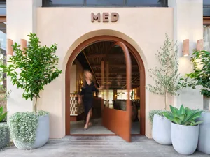 Warm and inviting restaurant entrance with a wooden frame, potted plants, and comfortable seating for guests