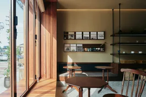 A well-lit room with wooden floors and walls, featuring two dining tables, chairs, and scattered books, creating an inviting atmosphere for gatherings or relaxation