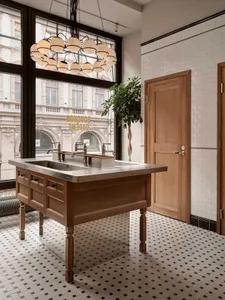 A bathroom with a sink in the center, a large window providing natural light, and two potted plants near the window, with three bottles on the countertop