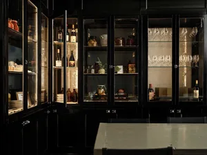 A cozy kitchen with a table in the center, wine glasses and bottles scattered throughout, and a warm atmosphere
