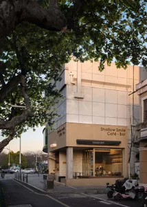 A modern cafe with a white concrete facade, large windows, and a urban atmosphere, surrounded by parked cars