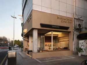 A warm and inviting cafe with a large window, seating areas, potted plants, and natural light