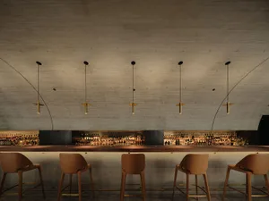 A modern bar with a long counter and stools, featuring multiple bottles and a stylish atmosphere