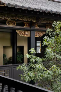 An Asian-style building with a balcony overlooking a garden area, featuring black pillars and gold accents, with potted plants adding to the serene ambiance