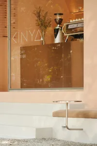 A cozy coffee shop interior with wooden furniture, a window display, and a potted plant, featuring two tables and chairs for seating