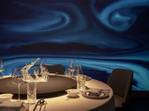 Elegant dining area with a round table set for dinner, featuring crystal glassware, multiple chairs, and various utensils