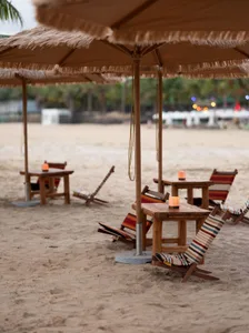 A relaxed beachside bar area with wicker chairs and tables under a large umbrella, perfect for a leisurely day near the ocean