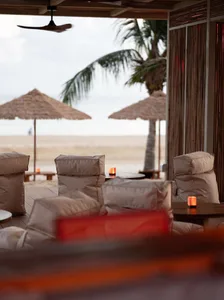 A beachside seating area with several couches and umbrellas on a wooden deck overlooking the ocean